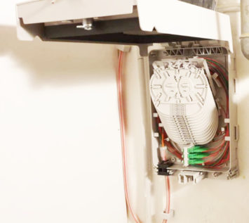 Ein an der Wand montierter Verteilerkasten für Glasfaser-Anschlüsse, dessen Deckel geöffnet ist und in dessen Inneren ordentlich geordnete Kabel, Stecker und Spleißfächer zu sehen sind - für Beratung und schnelles Internet.
