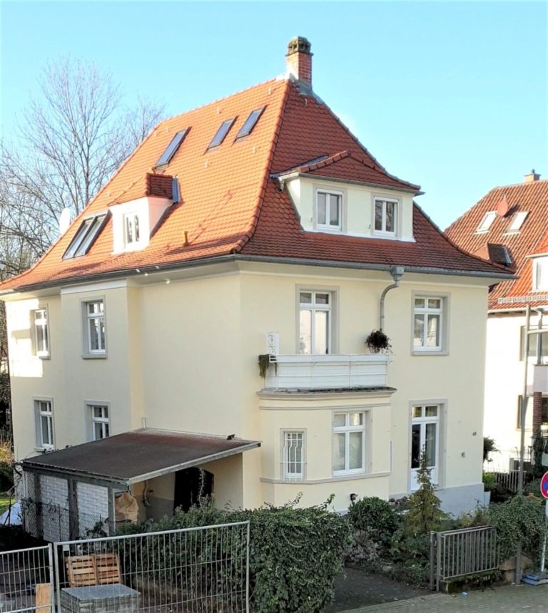 Ein dreistöckiges, cremefarbenes Haus mit rotem Ziegeldach, mehreren Fenstern, einem Balkon und einem kleinen überdachten Carport, umgeben von einem Zaun und Grünflächen - die perfekte Inspiration für 2D-Design- oder LaserCut-Projekte.